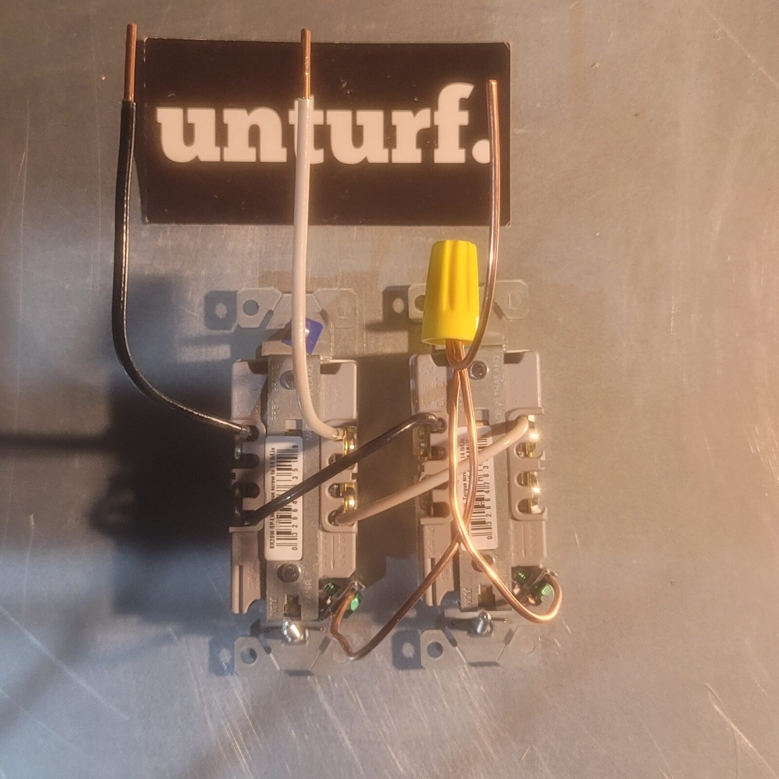 A pair of receptacles jumpered together with black, white & copper leads below an unturf sticker