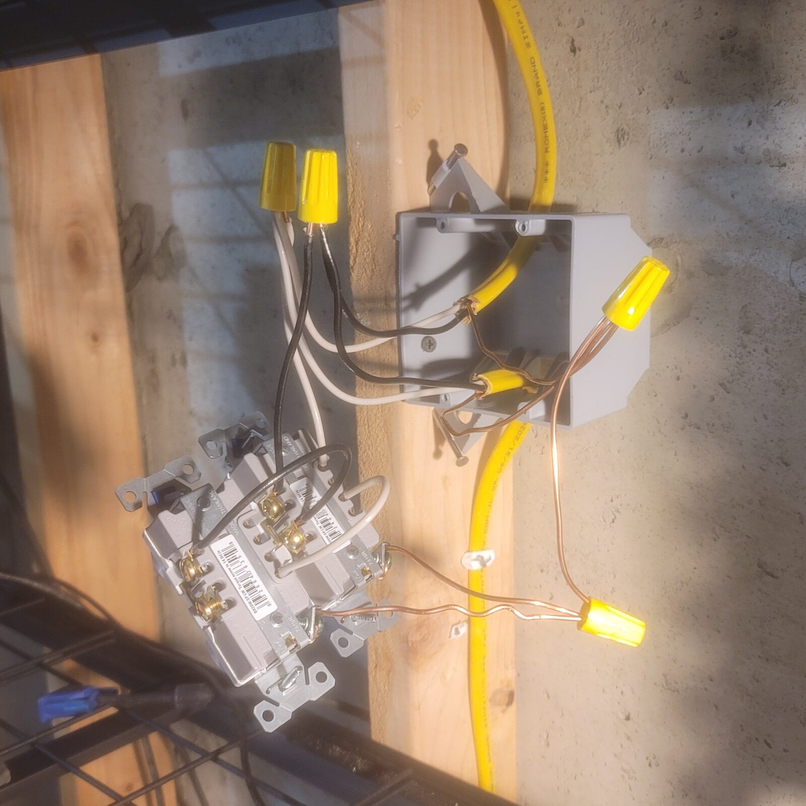A pair of wired receptacles hanging beside the box, pigtails joined to the feed with yellow wire nuts