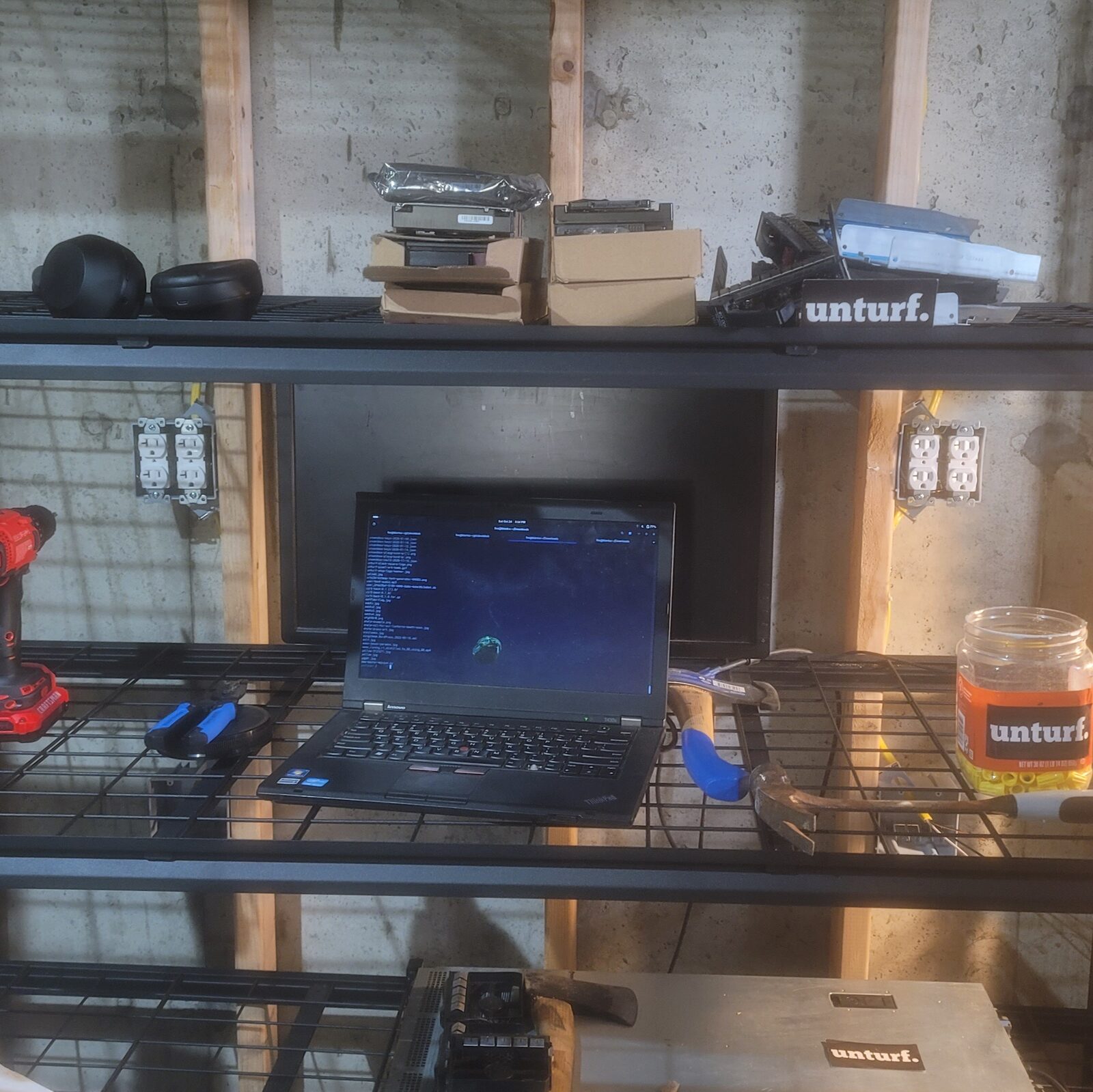 Steel shelving with a ThinkPad, tools, hard drives & receptacles on the wall behind